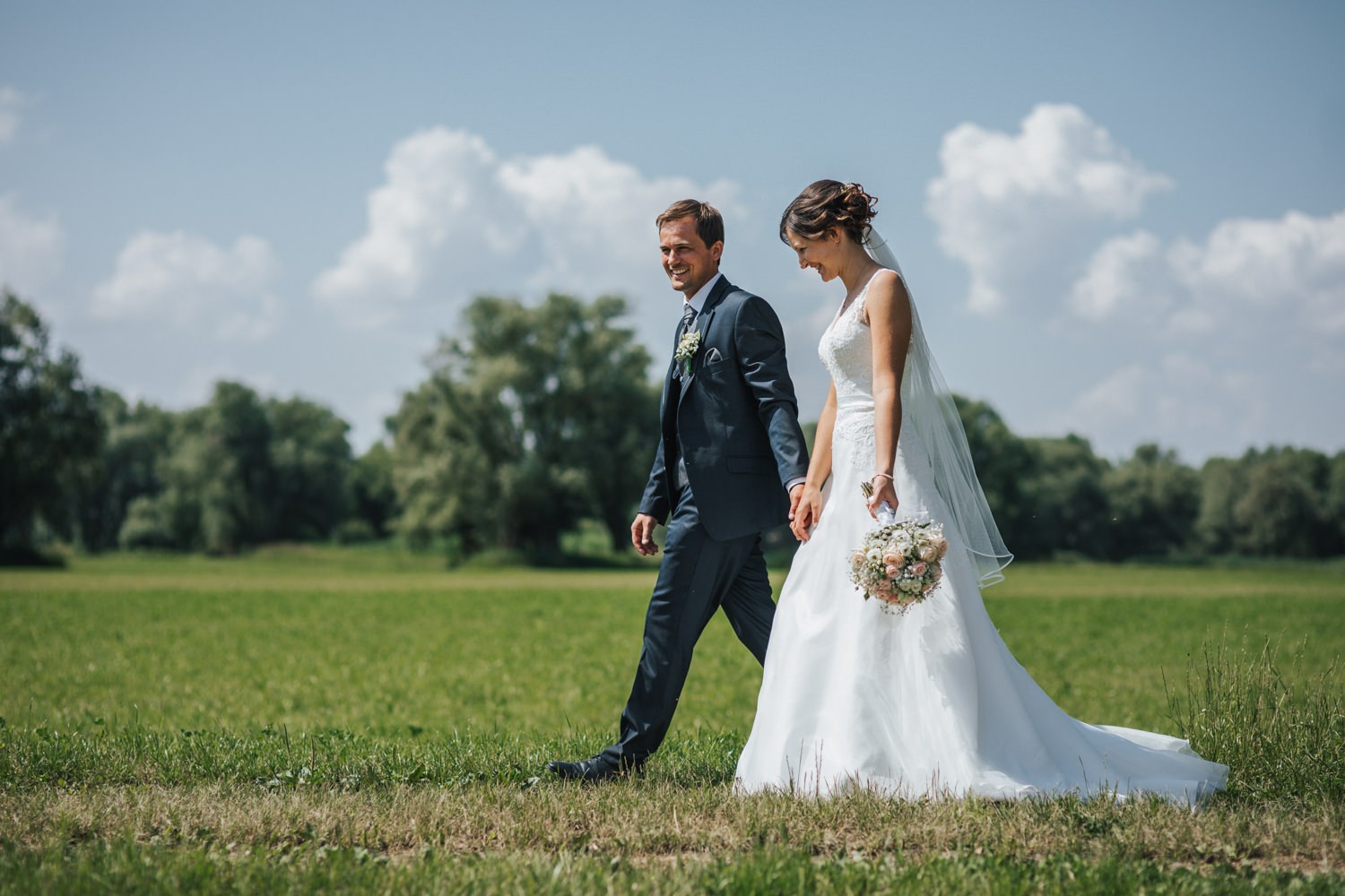 Hochzeit in Deggendorf, Paarshooting am Donauufer, Brautpaar läuft lachend einen Weg entlang
