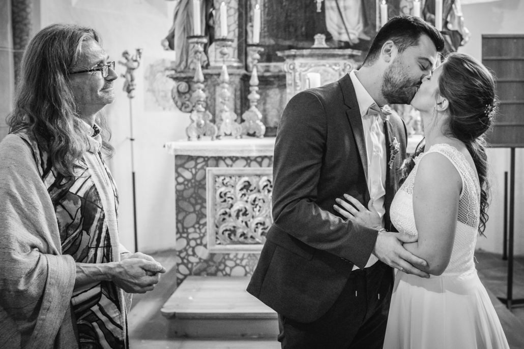 kirchliche Hochzeit in Grongörgen, Bad Birnbach, das brautpaar küsst sich, der Pfarrer schaut zu
