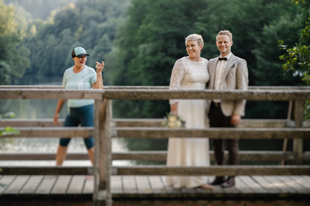 Hochzeit auf dem Rahaberghof, Oberösterreich, Paarshooting, Paar steht auf Brücke während Frau mit mahnendem Finger vorbei geht