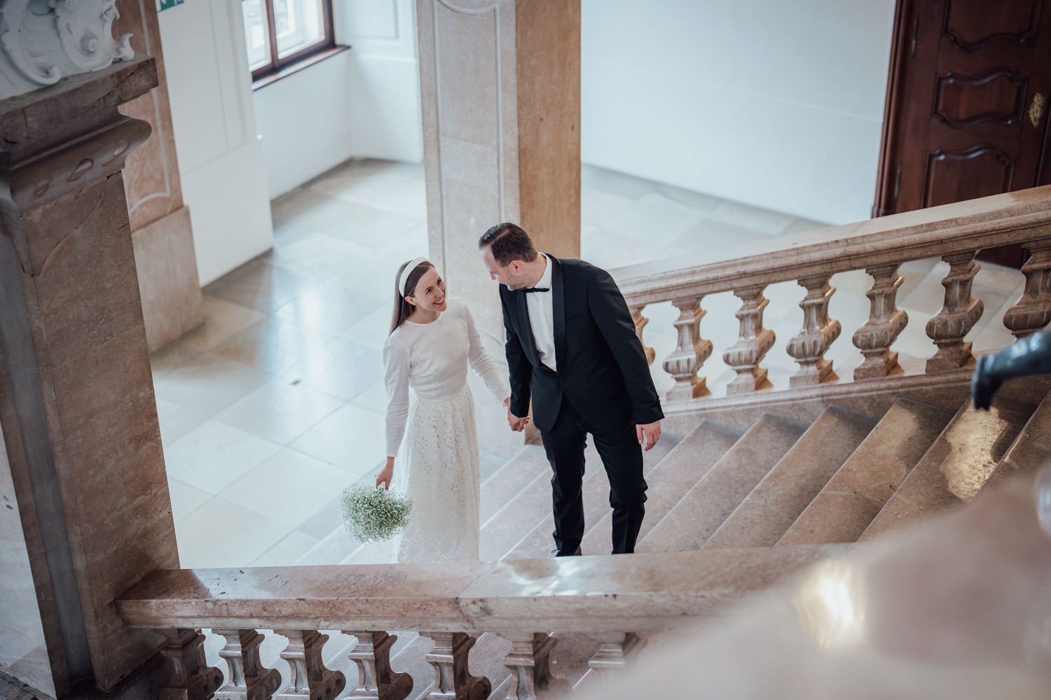 Ein Brautpaar läuft Hand in Hand die Treppe hinauf, der Bräutigam dreht sich zur Braut um