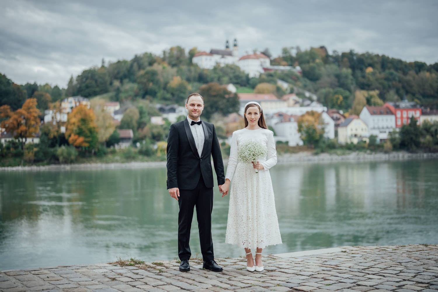 Brautpaar steht Hand in Hand am Innufer in Passau, im Hintergrund MariaHilf