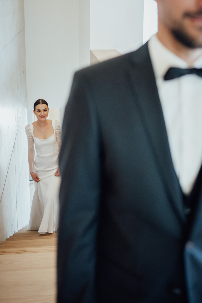 First Look Moment einer kirchlichen Hochzeit in Hutthurm – Braut nähert sich lächelnd von hinten.